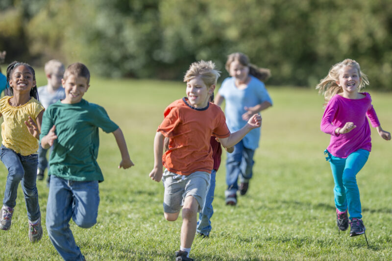 A large group of kids are seen running in a field (tag games)
