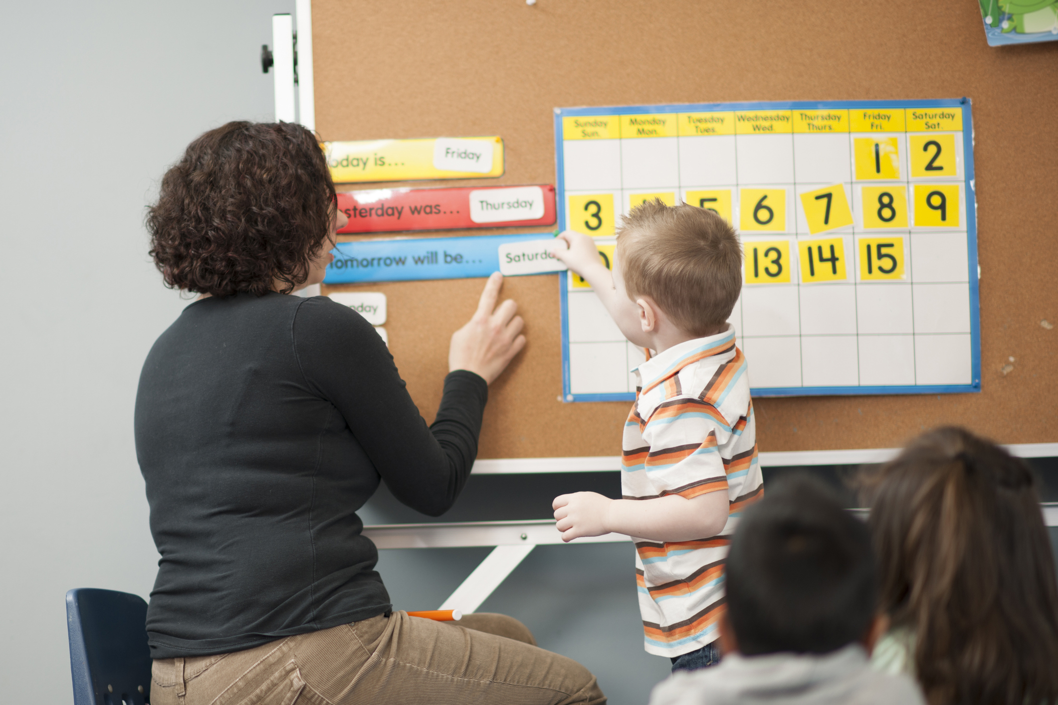 A multi-ethnic group of elementary age students are learning the days of the week with their teacher.