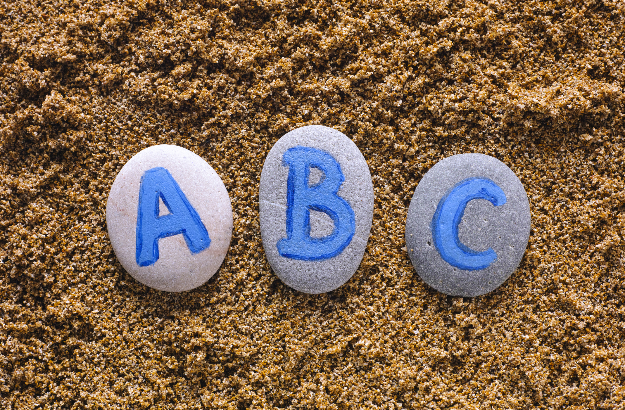 ABC letters drawn on stones spell out on sea sand. Letters drawn by me