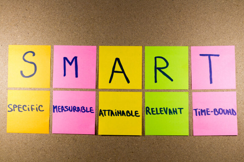 Set goals SMART (specific, measurable, attainable, recorded, timely) colorful sticky notes on cork bulletin board.