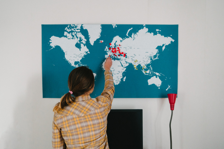 A woman stands in front of a world map putting a pin into it. 