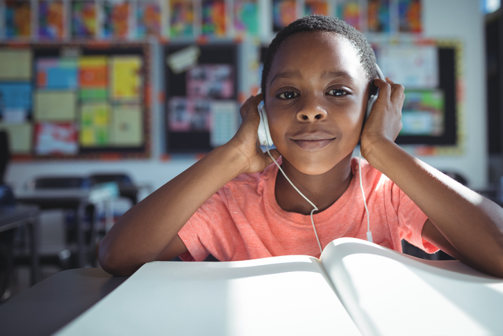 Calming classroom theme can be music as shown by this little boy sitting listening to music on earpods at a desk in a classroom.