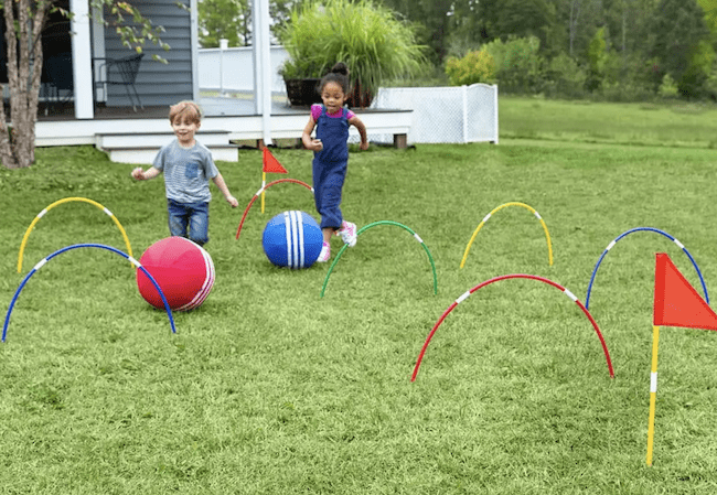 Two children playing a giant kick croquet game outside