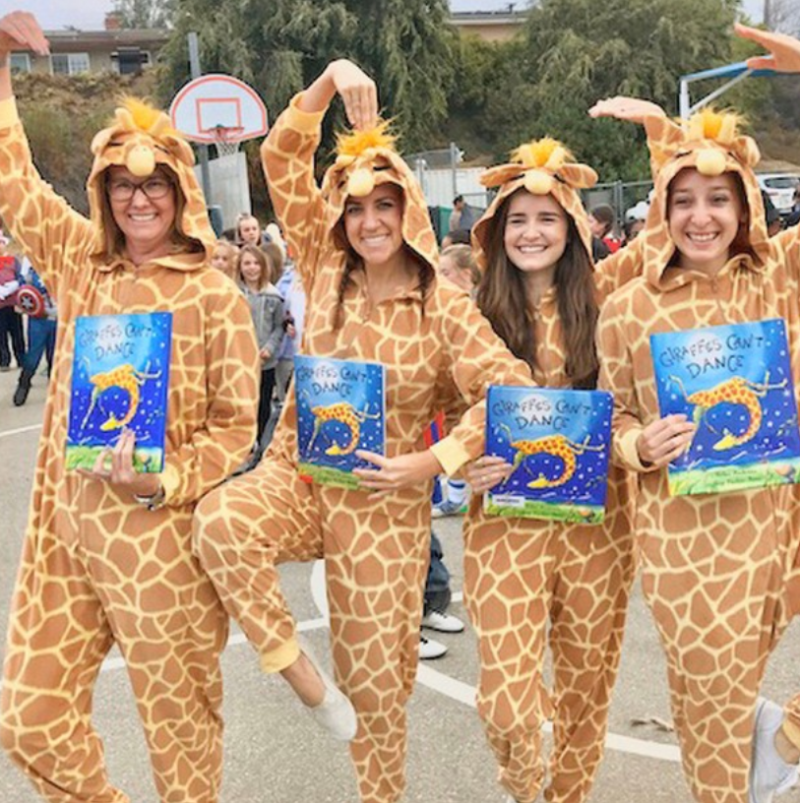 Several teachers are dressed in giraffe costumes and holding the book Giraffe's Can't Dance