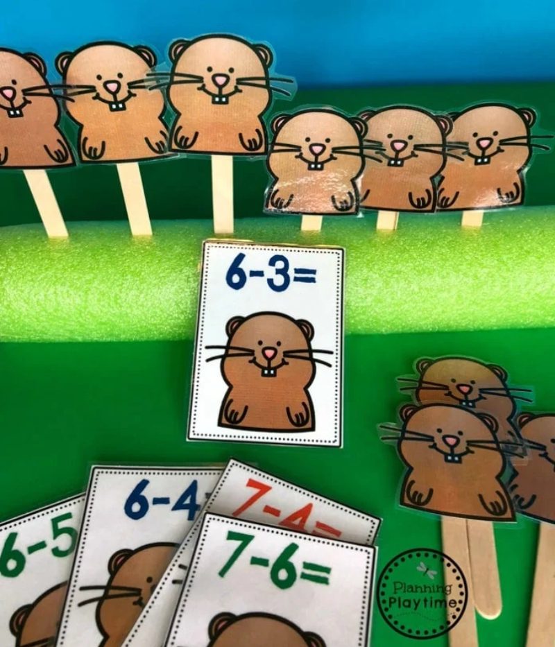 popsicle stick gopher puppets sticking out of a green pool noodle and subtraction problem cards