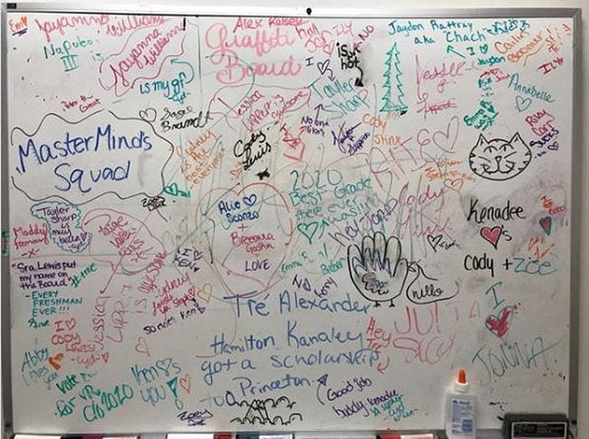 A whiteboard decorated with colorful graffiti by students