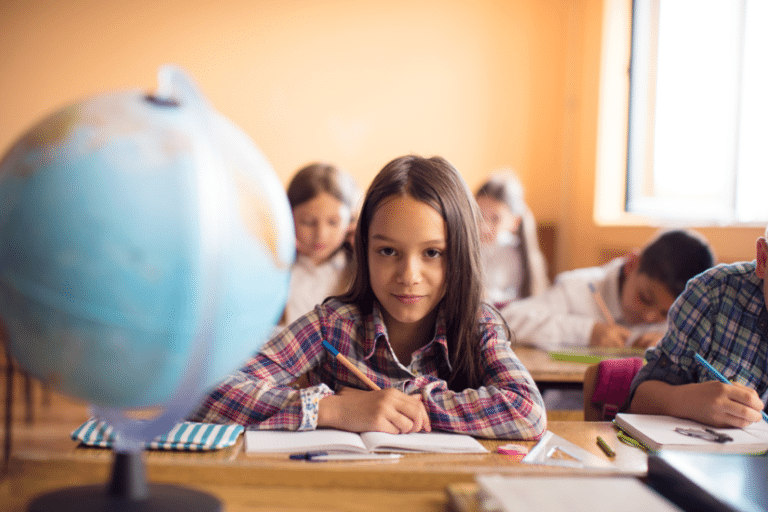 Young girl in classroom writing and looking at a globe – Simple Social Studies Activities That Incorporate Reading and Writing