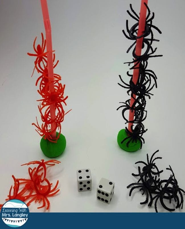 Plastic spider rings stacked onto drinking straws stuck into clay, with pair of dice