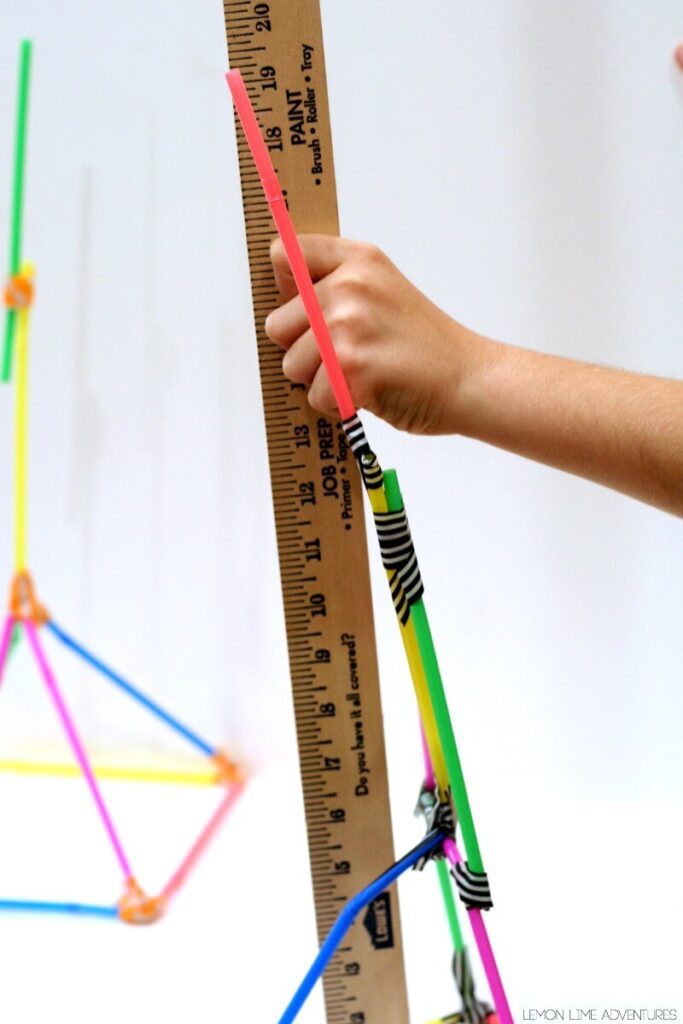 Students hands building a tower with colored drinking straws and a ruler measuring height.