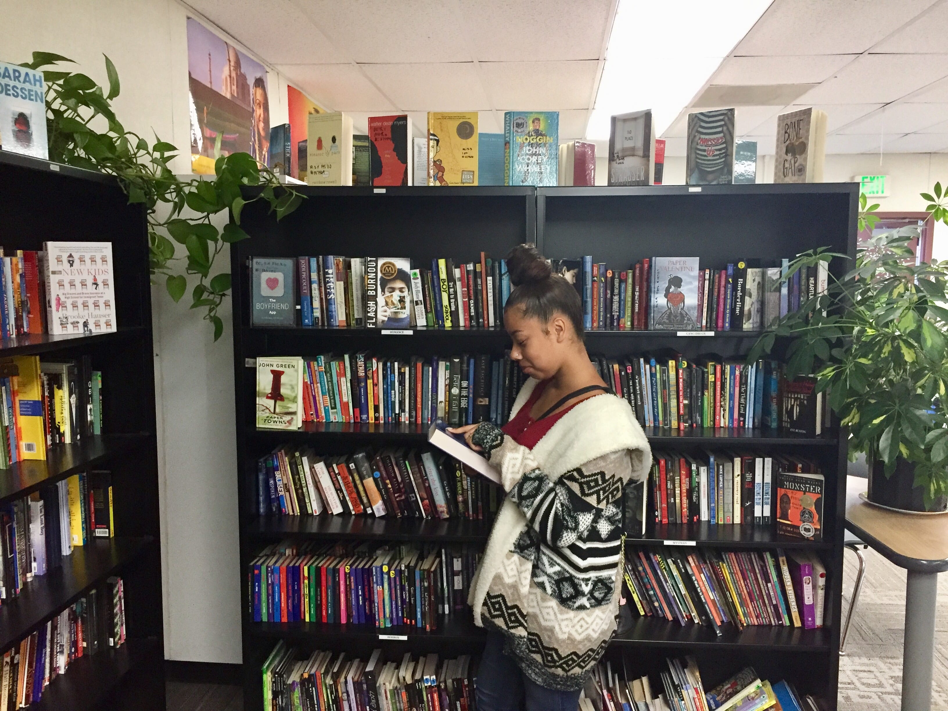 Student standing in front of bookshelves reading a book - help struggling readers