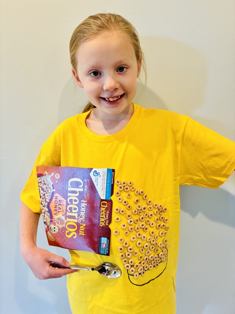 a student wearing a yellow shirt with a box of cheerios and a spoon with 100 cheerios to celebrate 100 days of school