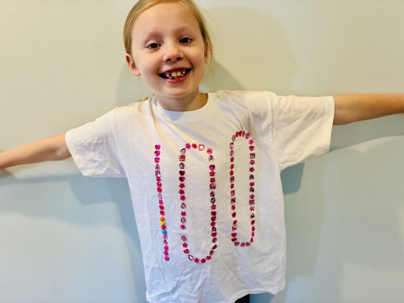 a student wearing a white  shirt with the number 100 outlined in jewels to celebrate the 100th day of school