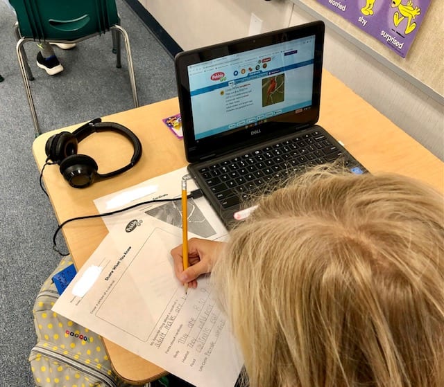 Student completing the cardinal activity sheets while reading information on PebbleGo