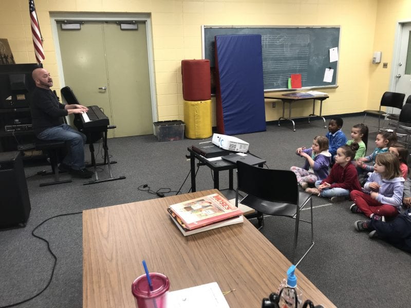 Music teacher playing keyboard while students listen to a song from Carnegie Hall Musical Explorers program