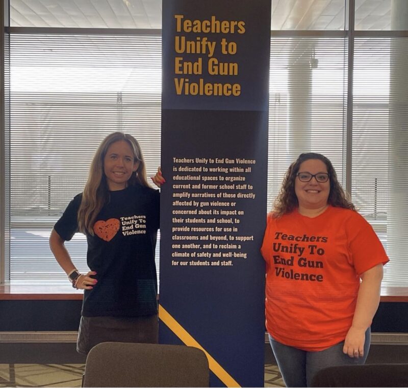 Sari Beth Rosenberg and a fellow co-founder of Teachers Unify to End Gun Violence pose next to a standard.