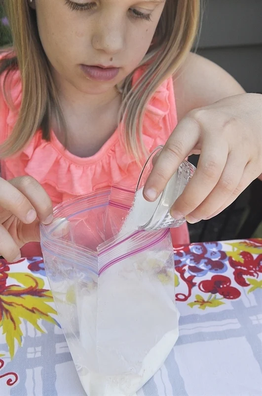 A girl in a pink blouse making ice cream in a Ziploc bag