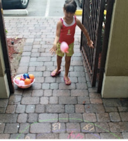 girl throwing water balloons at numbers written in chalk on the pavement for a water activity 