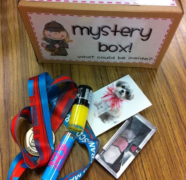Cardboard box labeled Mystery Box with items like nail polish, photos, medal on a ribbon, and more