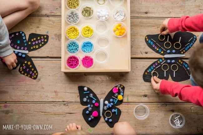 Young students adding beads, pom poms, and other embellishments to black paper butterflies