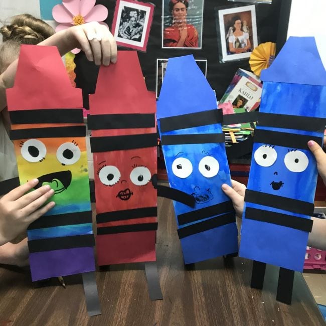 Students holding colorful oversized paper crayons with smiley faces (Kindergarten Art)