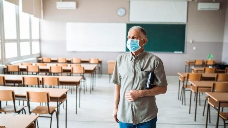 An older man wearing a mask in an empty classroom.