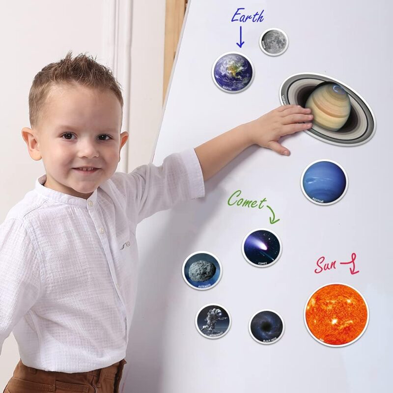 A little boy stands in front of a white board that has magnetic planets on it in this example of solar system projects.
