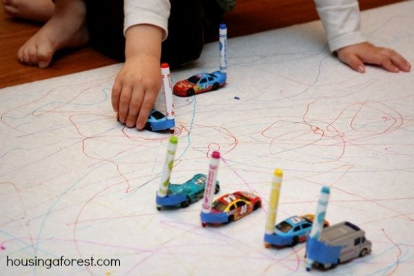 Child using matchbox cars with markers taped to the front to draw on a piece of paper