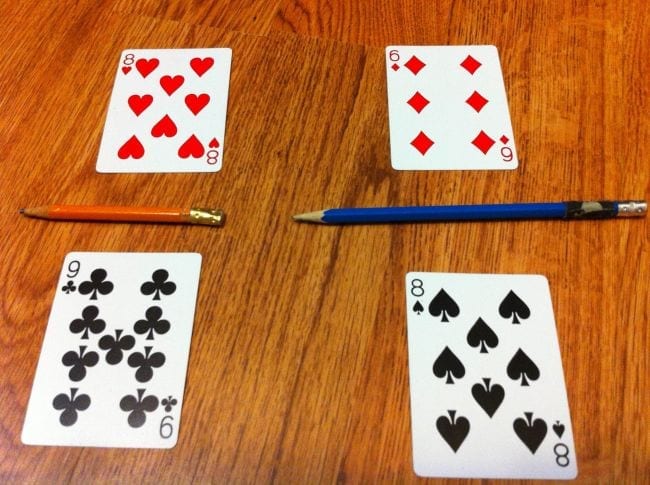 Two sets of playing cards laid out with pencils to create fractions