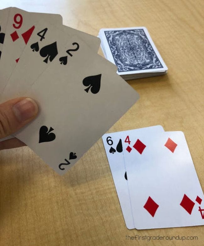 Student holding playing cards with two cards adding up to 10 laid face up on the table