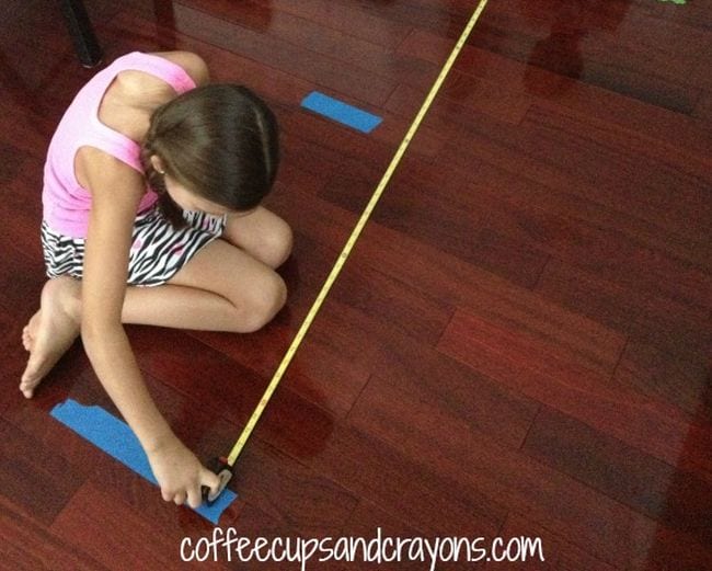 A girl sits on the floor measuring the distance between pieces of blue tape