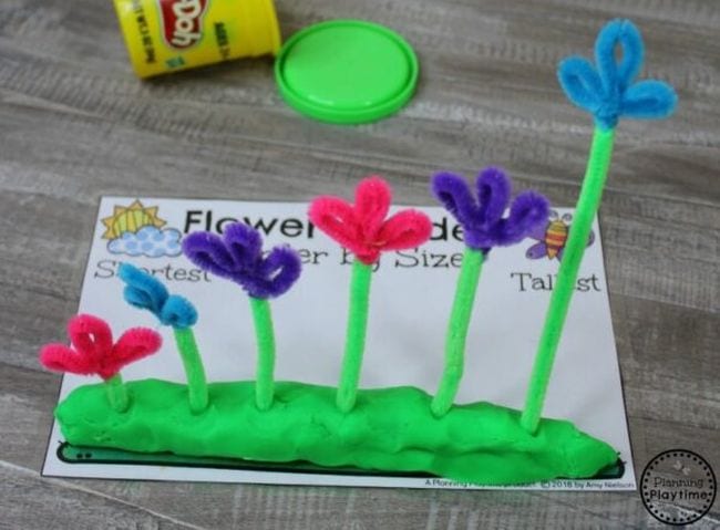 Colorful pipe cleaner flowers are stuck into green playdough as an example of measurement activities