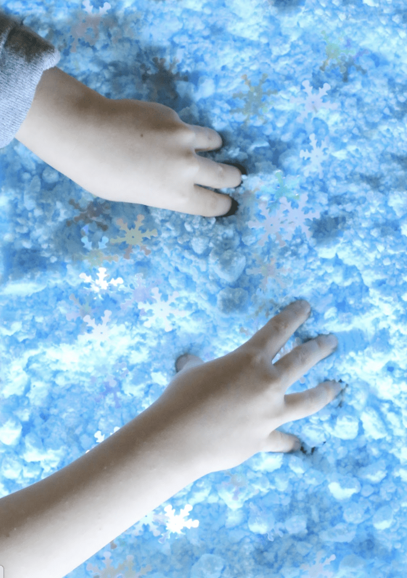 a student's hands playing in fake blue snow. 