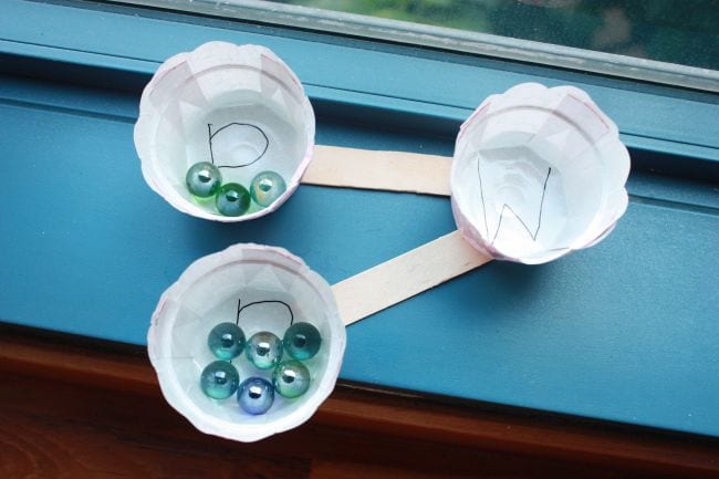 Three cupcake wrappers connected by wood craft sticks, with marbles in two of the sections (Number Bonds Activities)