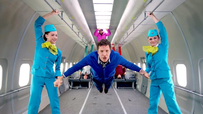 OK Go music video, a man floating with two women on either side of him.