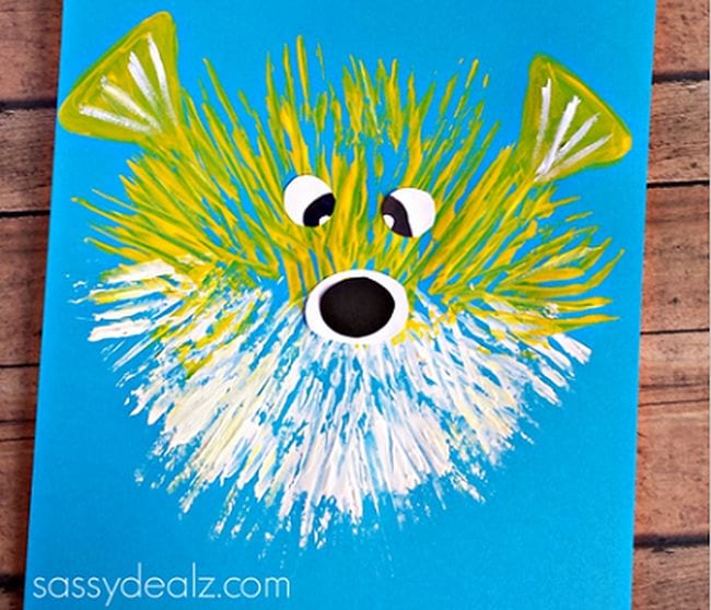 A puffer fish has been painted on a blue background using yellow and white paint. A fork has been used to make the fins.