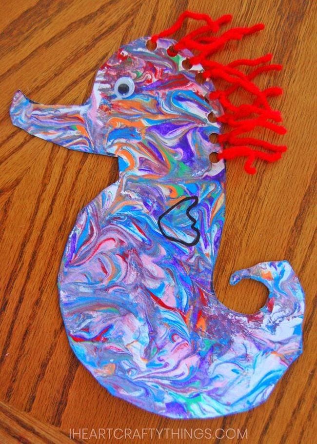 A colorful seahorse craft is shown. It has a googly eye. Holes have been punched in the head and red yarn has been strung through it (ocean activities)