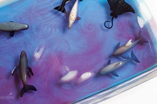 A tub of purplish, blue water has plastic whales and sharks in it (ocean activities)