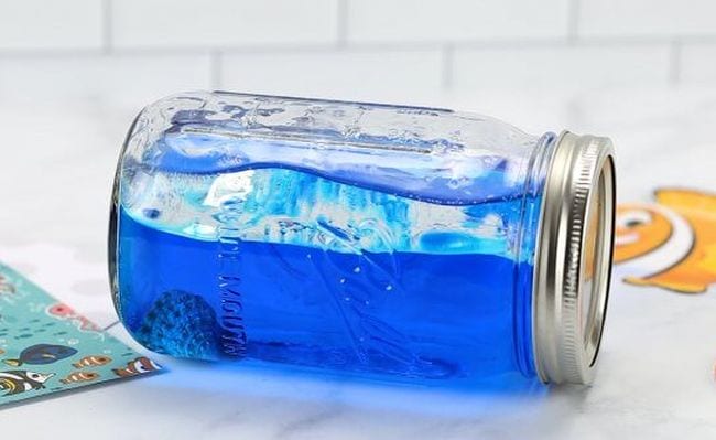 A Mason jar is laying on its side and filled with blue water.