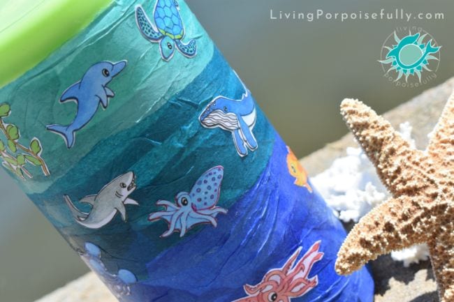 A jar is covered in blue crepe paper and has sea creature stickers on it.