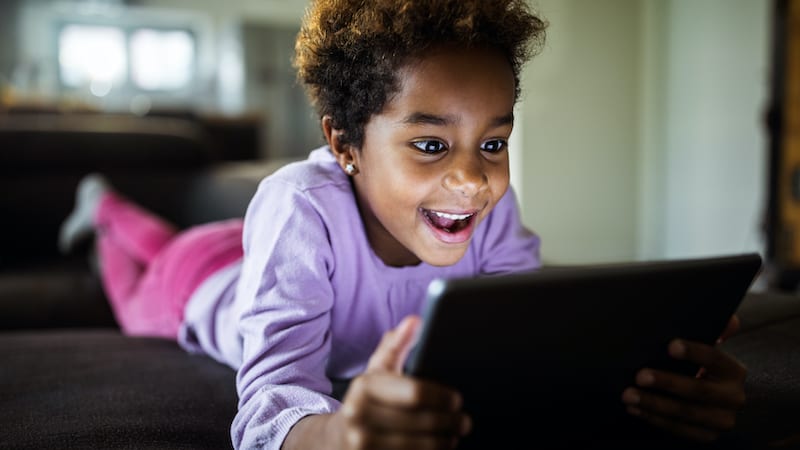Smiling girl lying on sofa and reading on her digital tablet.