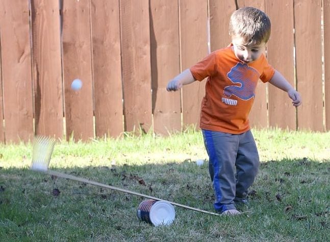 Child stomping on one side of a catapult made with a can and board, launching a ping pong ball into the air
