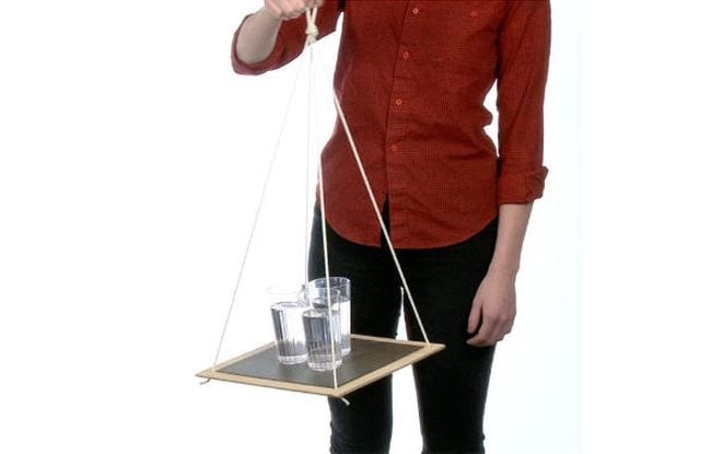 Woman holding a board suspended at the corners from string, with three glasses of water on the board (Outdoor Science)