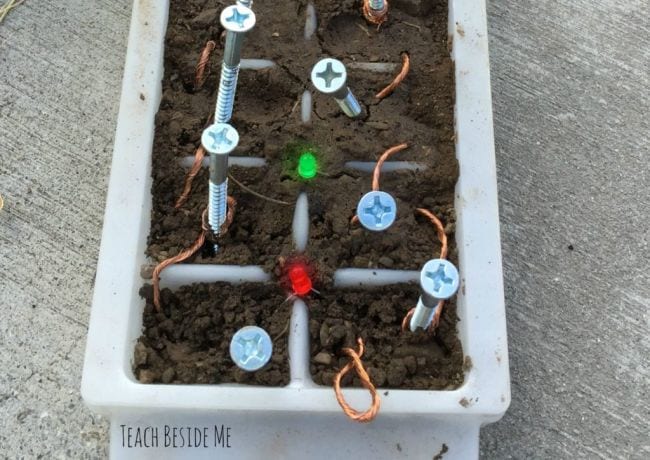 Outdoor science activities often involve dirt like this Ice cube tray filled with dirt, with screws and copper wire and small LEDs