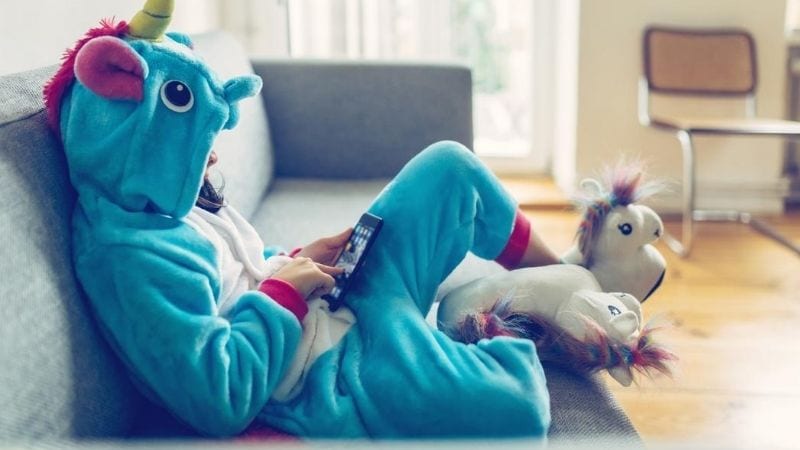 A young girl dressed up in a unicorn costume while playing on her phone.
