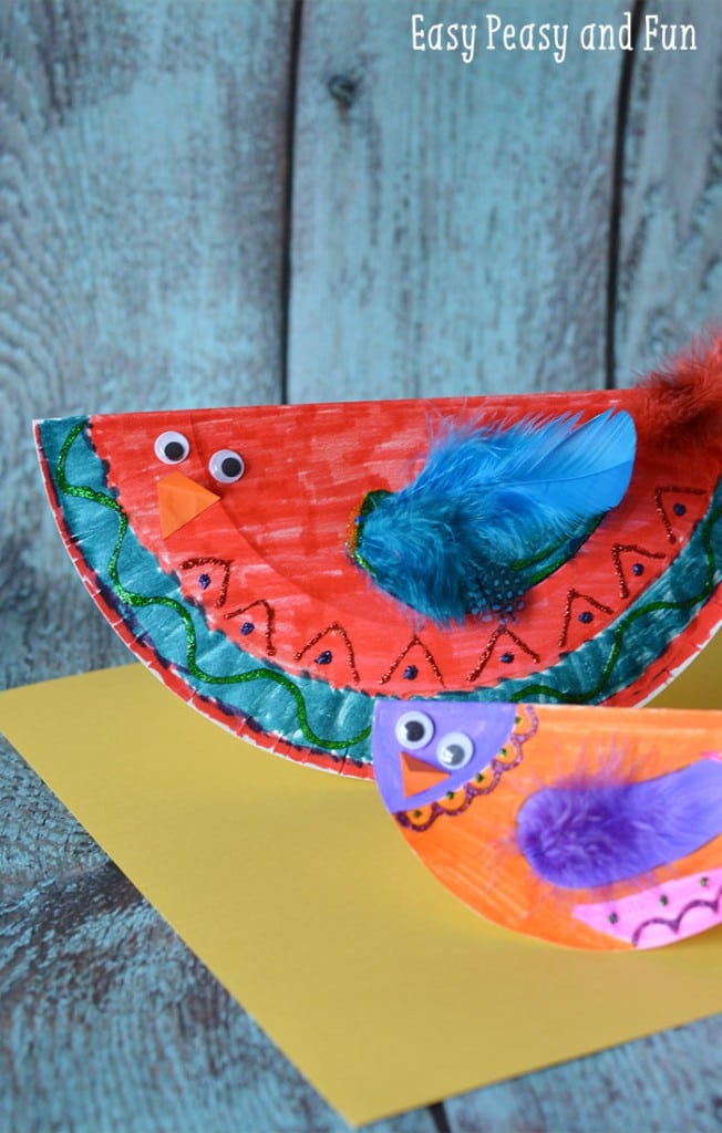 Colorful birds are made from decorated paper plates folded in half with googly eyes and a feather wing attached