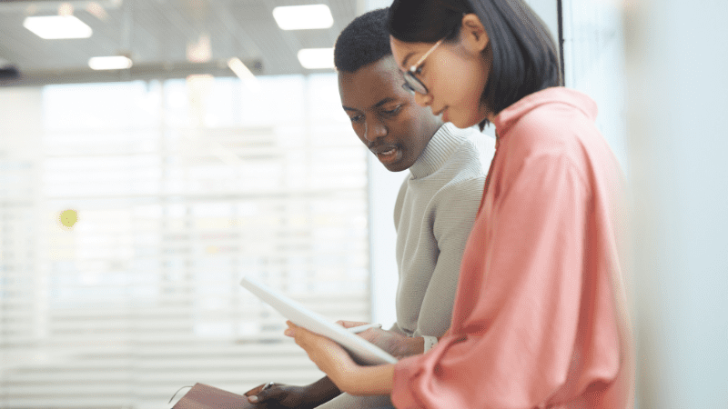 Young Black man and young Asian woman look over a paper together