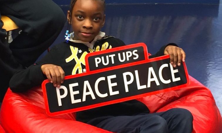 Girls sitting in red bean bag chair holding Peace Place street sign, as an example of SEL activities