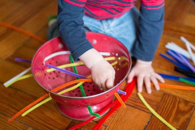 A child sits threading pipe cleaners through a container in this example of pipe cleaner crafts.