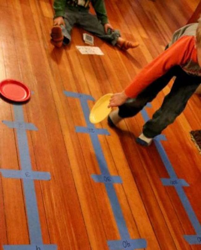 Young student moving colorful paper plates along number lines made from blue painter's tape on the floor