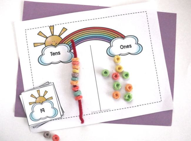 Worksheet with rainbow and clouds on each end, labeled ones and tens, with pipe cleaner strung with Froot Loops and handful of loose cereal